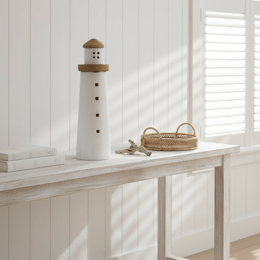 Decorative lighthouse with a white body and wooden top sitting on a console in a coastal hamptons beach house