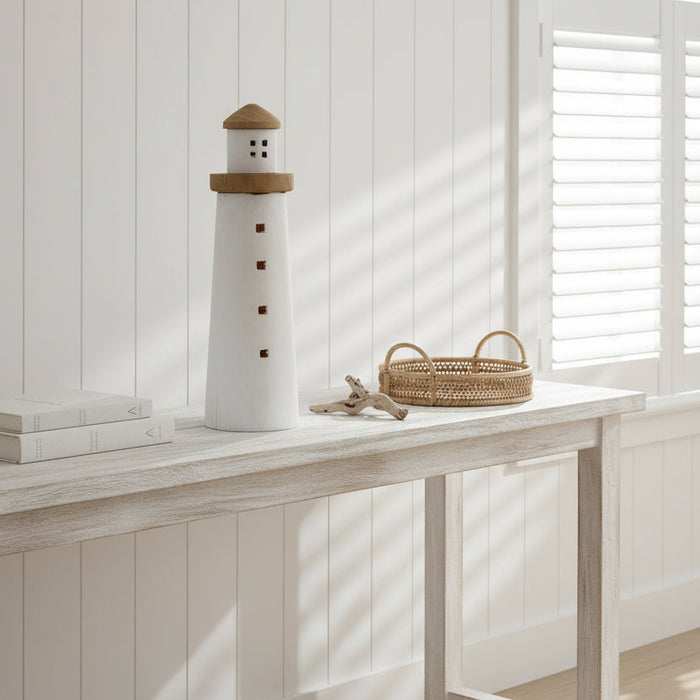 Decorative lighthouse with a white body and wooden top sitting on a console in a coastal hamptons beach house