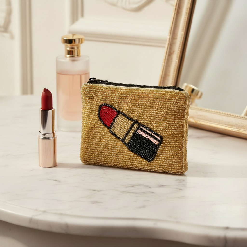A small zippered pouch made of gold-toned beaded material, featuring a large embroidered lipstick motif on the front in red, black, beige, and white, shown against a plain white background.