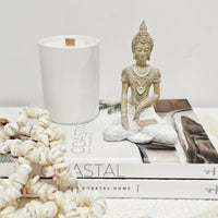 Decorative setting with a Buddha statue, candle, and books on a white surface