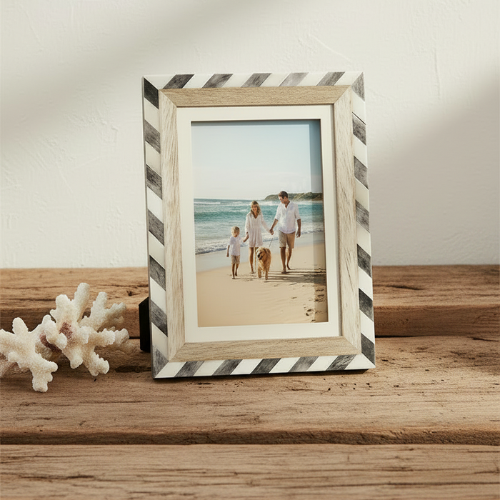 A rectangular picture frame with a striped border in black and white, featuring a light natural wood inner frame and a cream mat. 