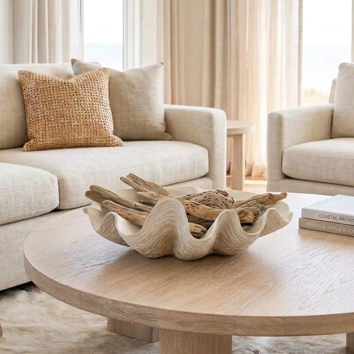 white resin clam shell styled with driftwood on a round coffee table in a neutral coastal home